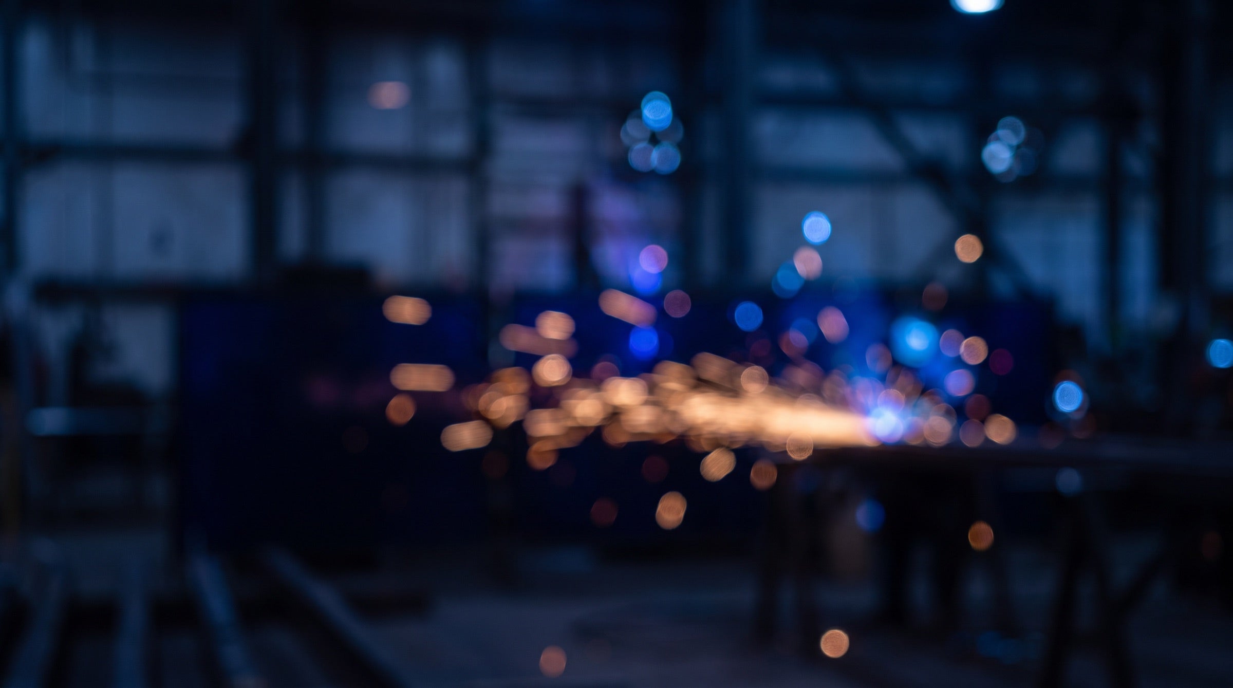 Blurred blue and amber welding sparks glowing in a dim workshop, a moody industrial texture